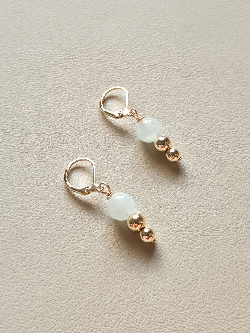 Pair of earrings with gold and light blue beads on a beige background