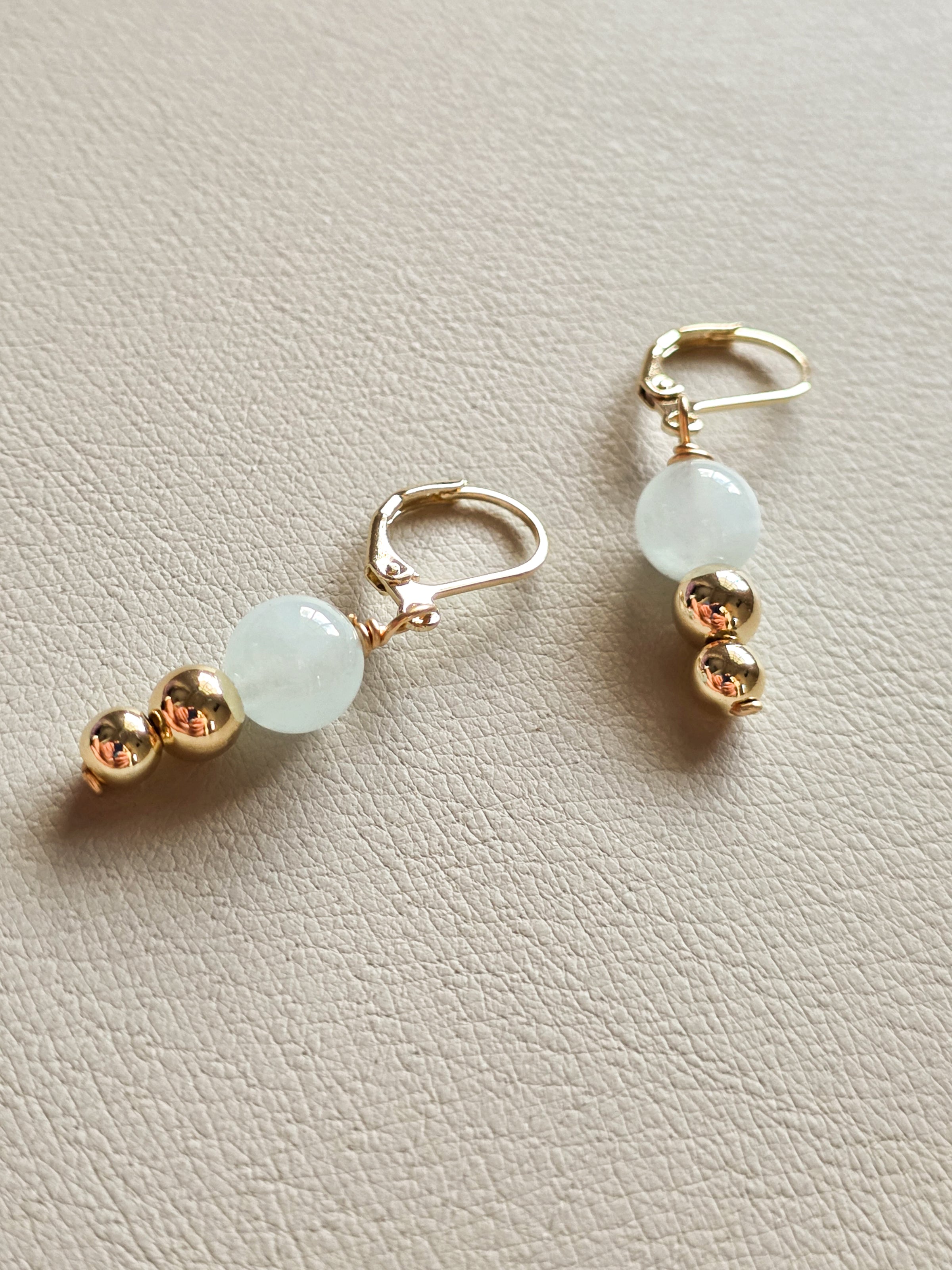 Pair of earrings with gold and light green beads on a beige background