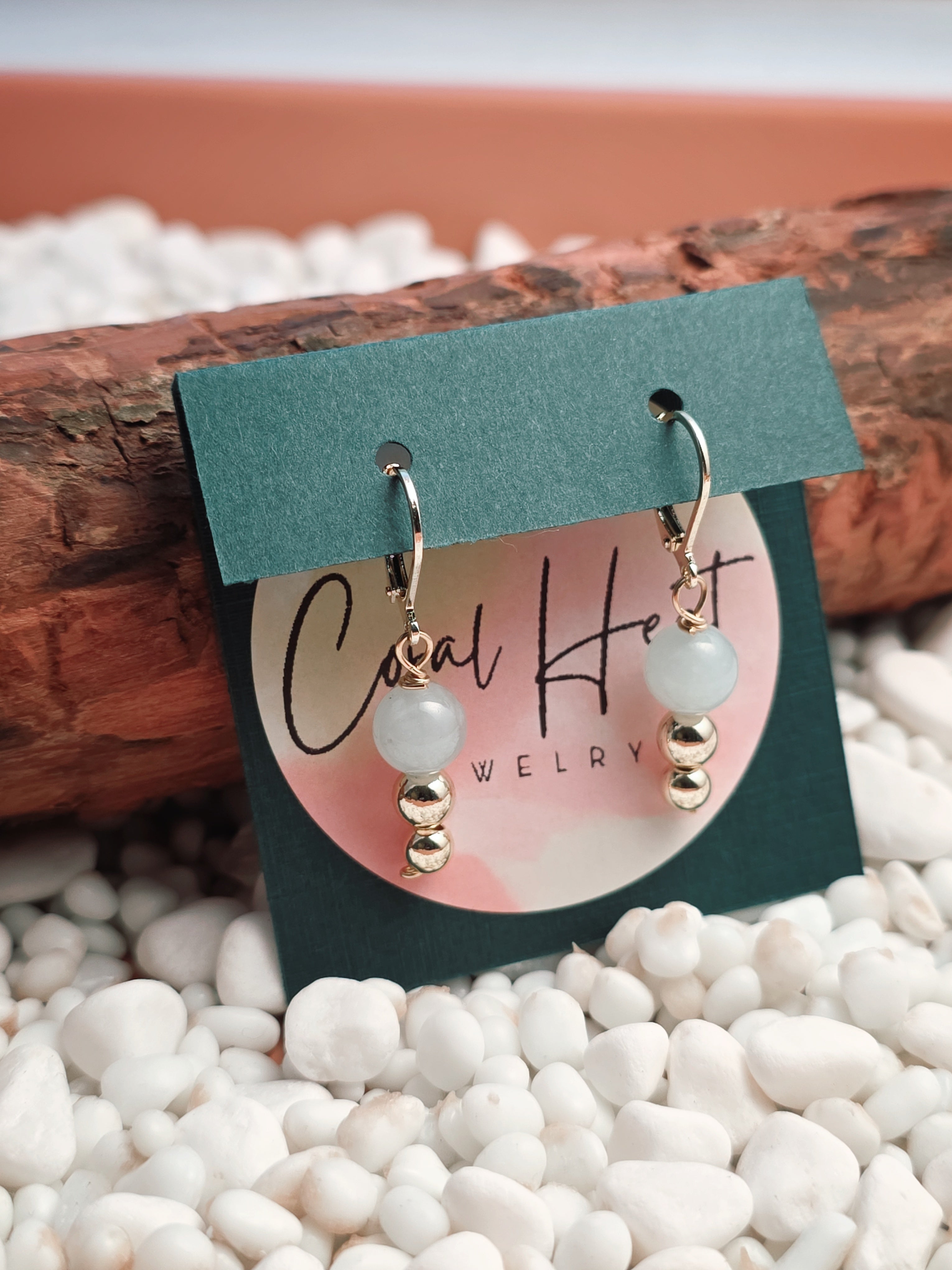 Pair of earrings on a display card with 'Cool Heat' branding, set against a natural stone background.