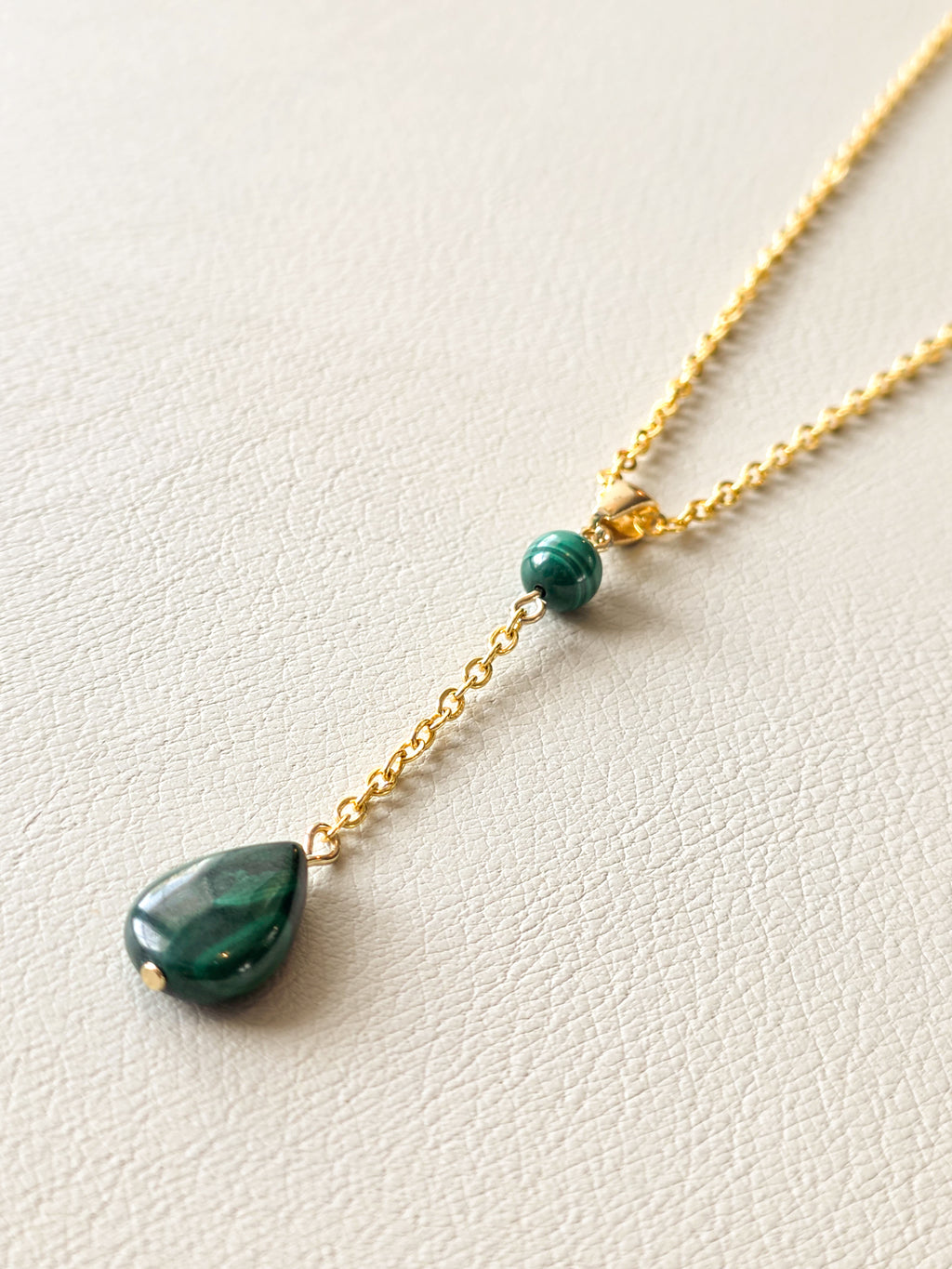 Close-up of a gold chain necklace with a green malachite bead and dangling malachite teardrop pendant.