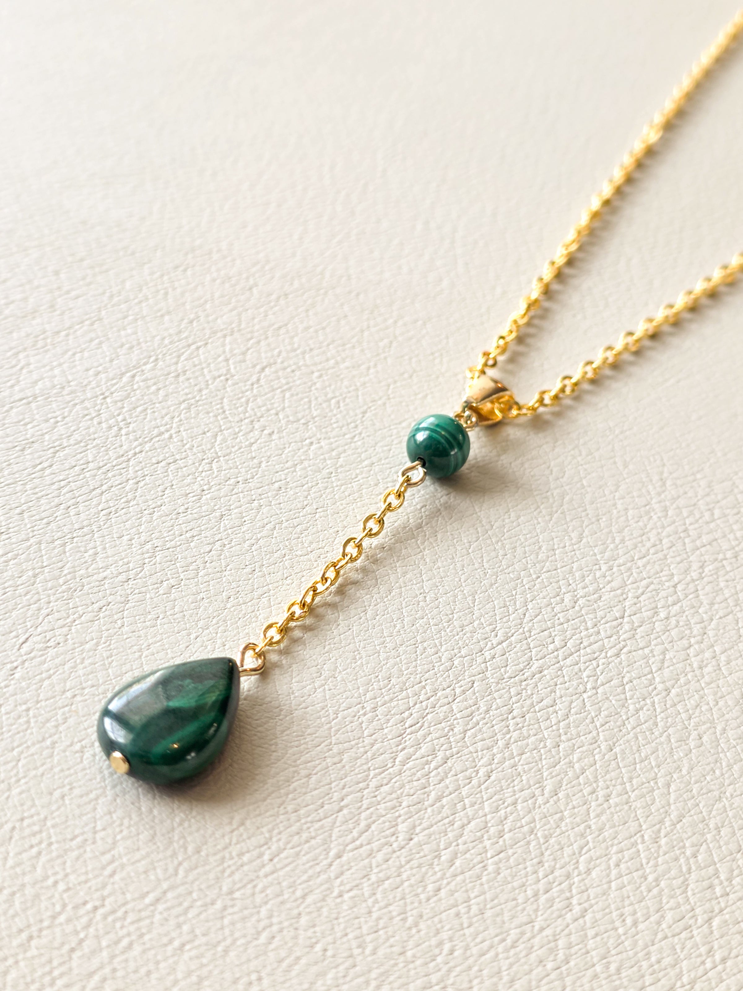 Close-up of a gold chain necklace with a green malachite bead and dangling malachite teardrop pendant.