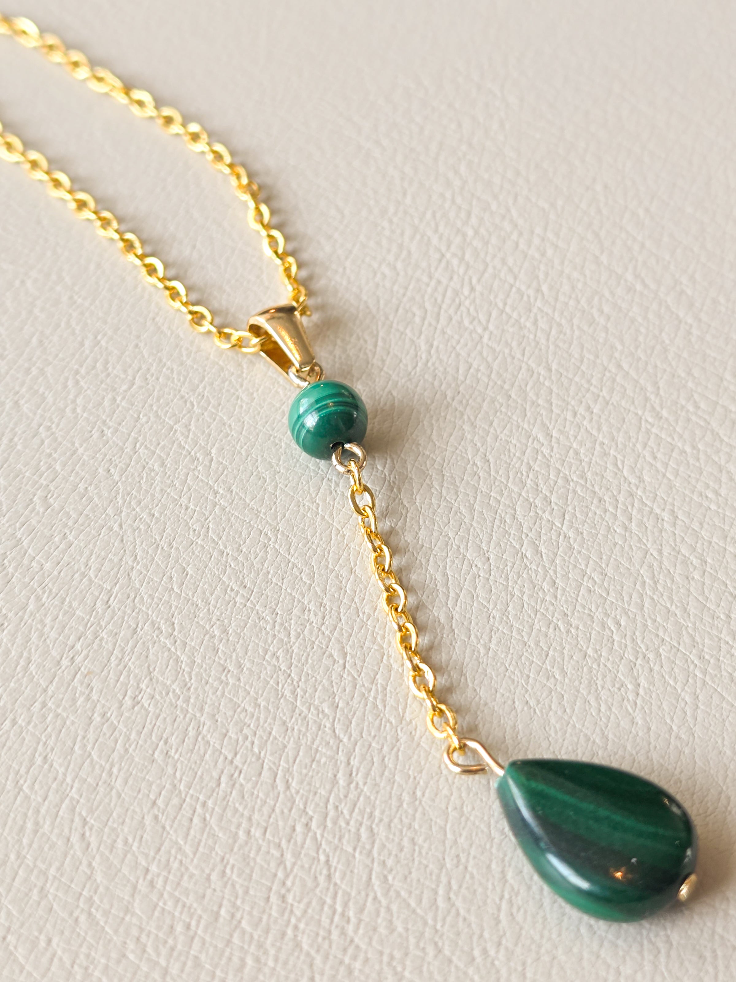 Close-up of a gold chain necklace with a green malachite bead and dangling malachite teardrop pendant.