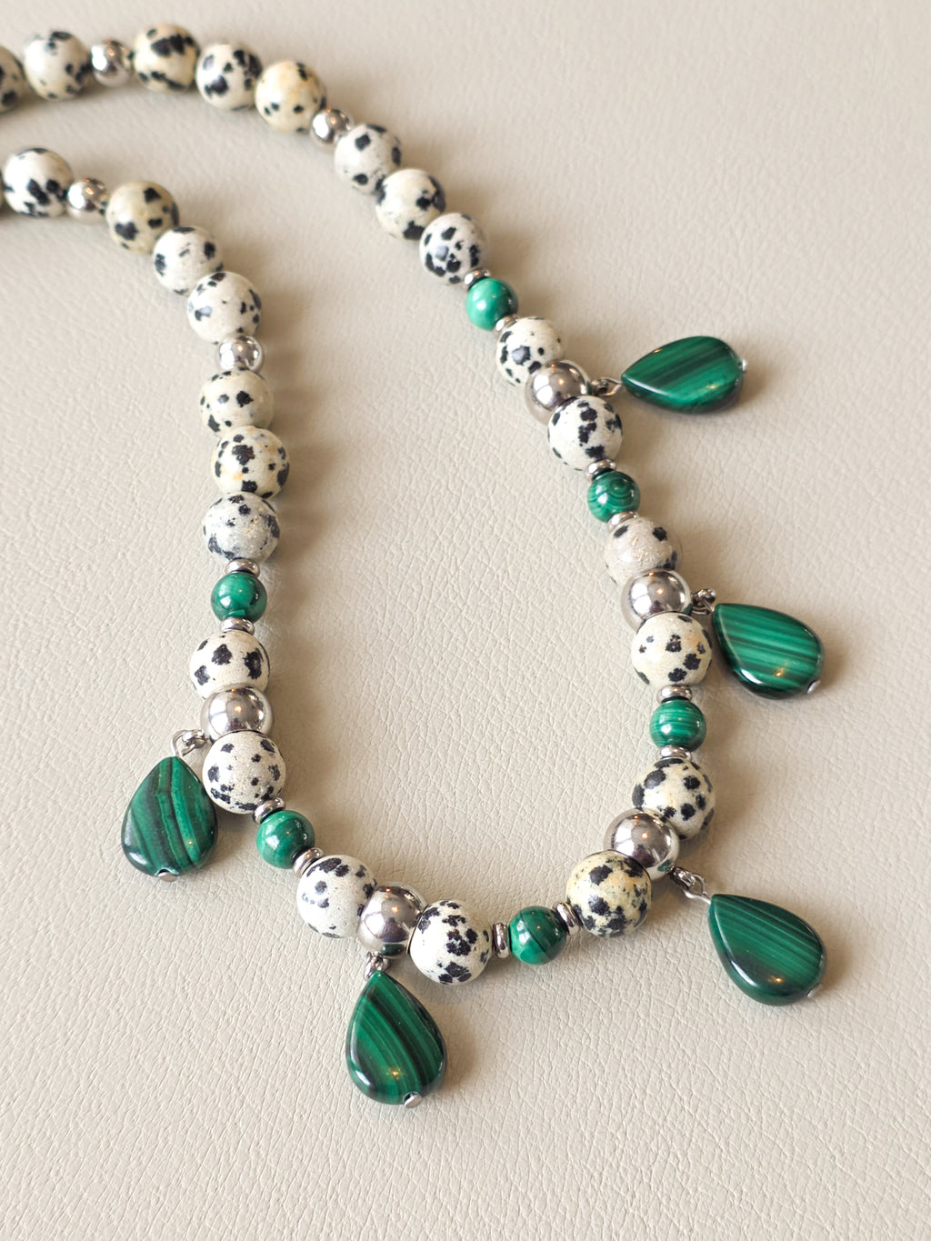 Close-up of speckled Dalmatian Jasper beads, green malachite accents, silver filled beads, and teardrop pendants.