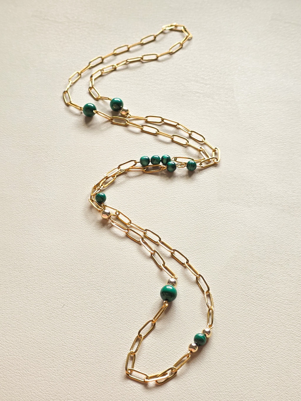 Gold chain necklace with green malachite beads on a light beige background